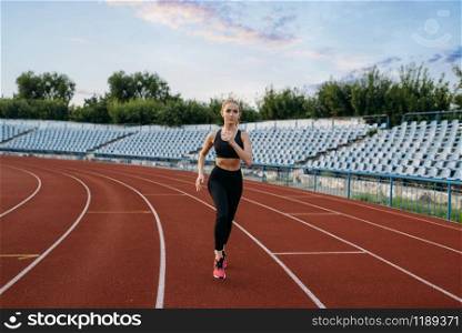 Female jogger in sportswear running, training on stadium. Woman doing stretching exercise before jogging on outdoor arena