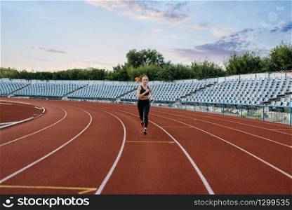 Female jogger in sportswear running, training on stadium. Woman doing stretching exercise before jogging on outdoor arena. Female jogger running, training on stadium