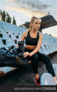 Female jogger in sportswear sitting on tribune, training on stadium. Woman doing stretching exercise before running on outdoor arena. Female jogger in sportswear sitting on tribune