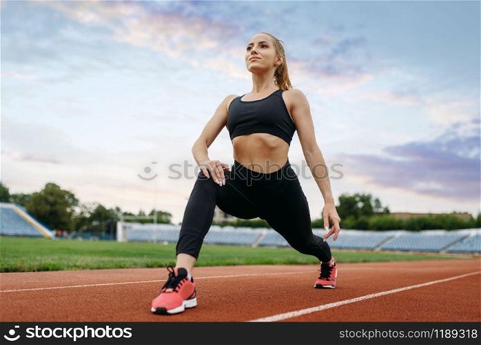 Female jogger in sportswear, training on stadium. Woman doing stretching exercise before running on outdoor arena