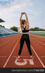 Female jogger in sportswear, training on stadium. Woman doing stretching exercise before running on outdoor arena. Female jogger in sportswear, training on stadium