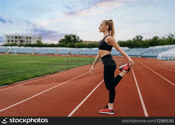 Female jogger in sportswear, workout on stadium. Woman doing stretching exercise before running on outdoor arena