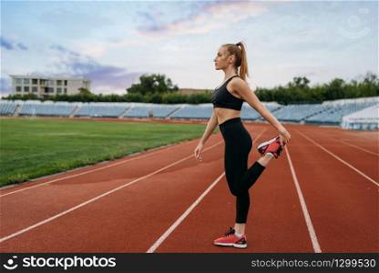 Female jogger in sportswear, workout on stadium. Woman doing stretching exercise before running on outdoor arena