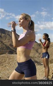 Female joggers drinking from water bottles, in mountains