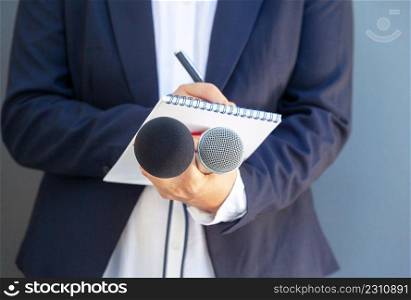 Female journalist at media event or press conference, writing notes, holding microphone
