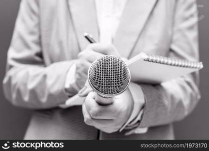 Female journalist at news conference or media event, writing notes, holding microphone