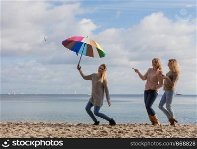 Female jumping with colorful umbrella her two friends are making fun of her laughing and looking.. Women making fun of jumping friend