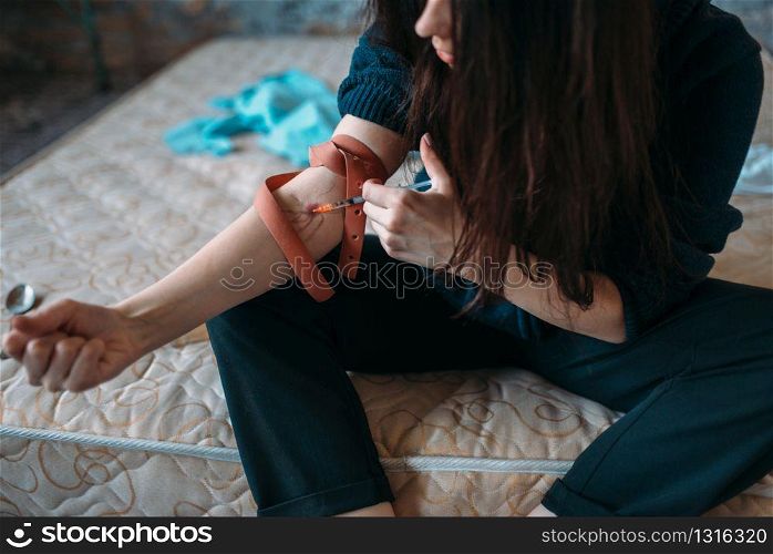 Female junkie with a syringe doing an injection dose in the arm. Narcotic addiction concept, drug addicted people. Female junkie with syringe doing an injection dose