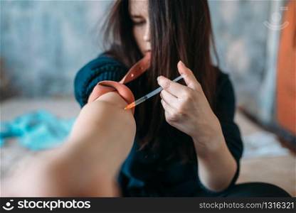 Female junkie with a syringe doing an injection dose in the arm. Narcotic addiction concept, drug addicted people. Female junkie with syringe doing an injection dose