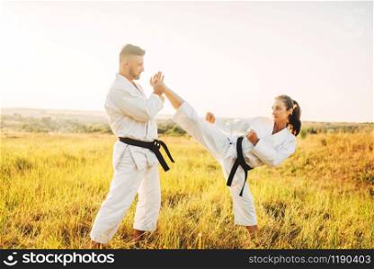 Female karate doing stretching exercise on training with male instructor. Martial art workout outdoor, technique practice, self defense. Female karate on training with male instructor