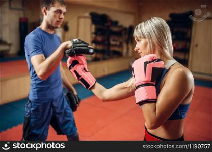 Female kickboxer in gloves practicing hand punch with male personal trainer in pads, workout in gym. Woman boxer on training, kickboxing practice. Female kickboxer practicing hand punch