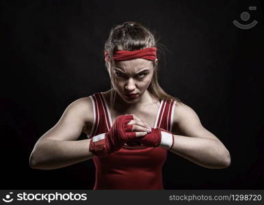 Female kickboxer in red gloves and sportswear, black background. Woman on boxing workout