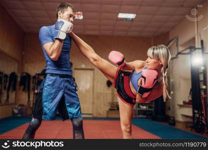 Female kickboxer practicing kicking with male personal trainer, workout in gym. Boxer strikes on training, kickboxing practice