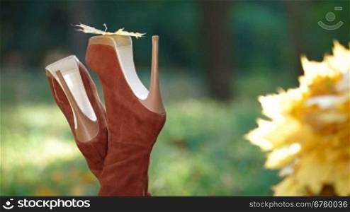 Female legs wearing high heel stiletto boots and autumn leaf