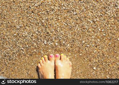 Female legs with bright pink and yellow nails on the sand in the sea water.