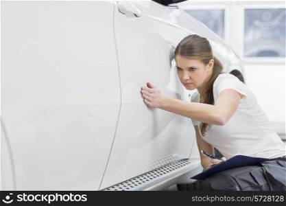 Female maintenance engineer examining car in workshop