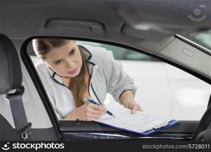 Female maintenance engineer with clipboard examining car&rsquo;s interior in workshop