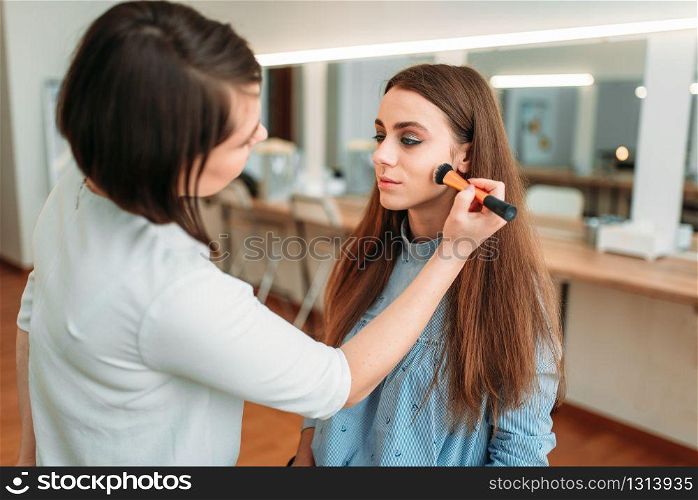 Female make up artist hand with brush applying make-up on beautiful girl face, beauty studio on background. Cosmetic salon. Female make up artist applying make-up with brush