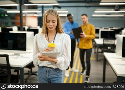 Female manager holds laptop and cup of coffee, IT office interior on background. Professional worker, planning or brainstorming. Successful employee in modern company. Female manager holds laptop and coffee, IT office