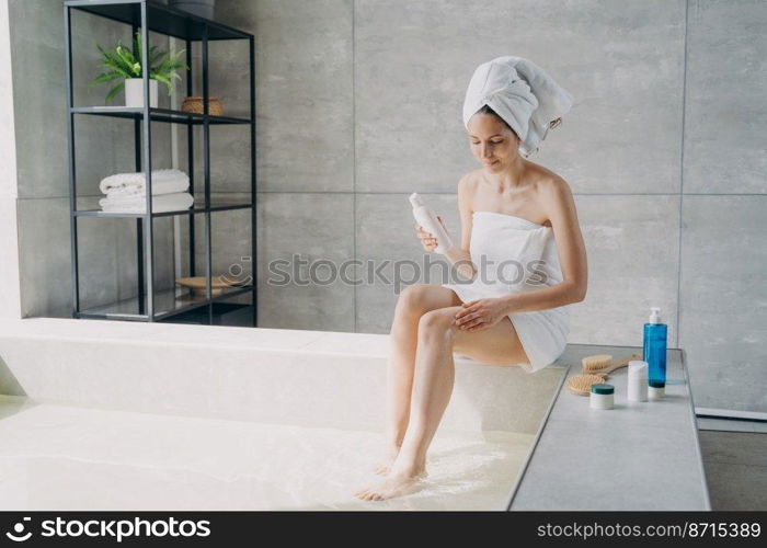 Female massaging legs with hand using natural anticellulite skincare lotion. Woman enjoy soft smooth silky skin during body care treatment procedure in bathroom. Self-care, spa cosmetics advertising.. Female massaging leg using natural anticellulite skincare cosmetics in bathroom. Body care treatment