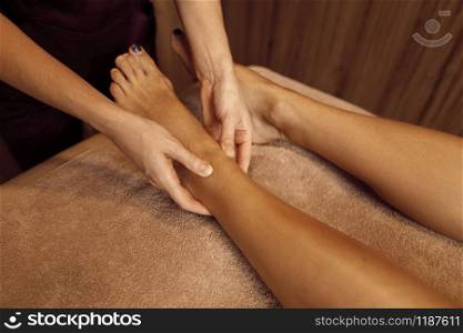 Female masseur pampering legs to young slim woman in towel, professional massage. Massaging and relaxation, body and skin care. Attractive lady in spa salon