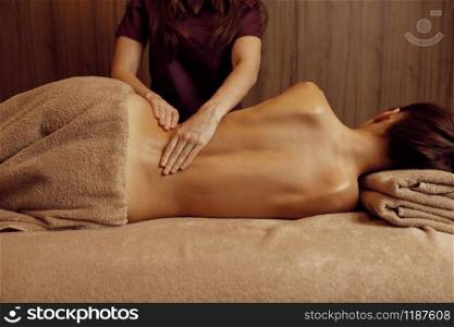 Female masseur pampering ribs to young slim woman in towel, professional massage. Massaging and relaxation, body and skin care. Attractive lady in spa salon. Female masseur pampering ribs to young slim woman