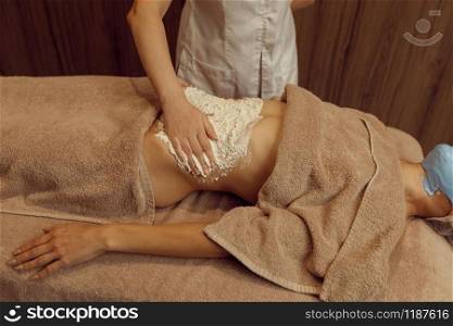 Female masseur rubbing cream on stomach of young slim woman in towel, professional massage. Massaging and relaxation, body and skin care. Attractive lady in spa salon. Masseur rubbing cream on stomach of slim woman