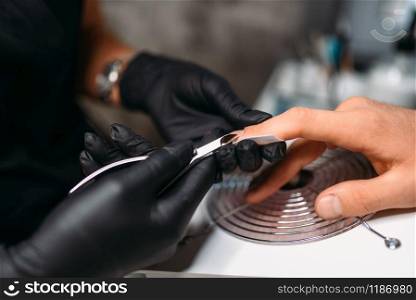 Female master in black gloves makes a man manicure in salon. Manicurist doing nail polishing. Female master makes a man manicure, nail polishing