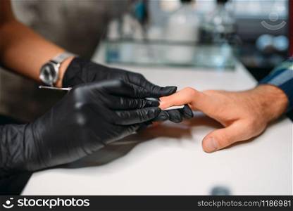Female master in black gloves polishing nails to male client, top view, men manicure in salon. Manicurist doing hands care procedure. Master in gloves polishing nails to male client