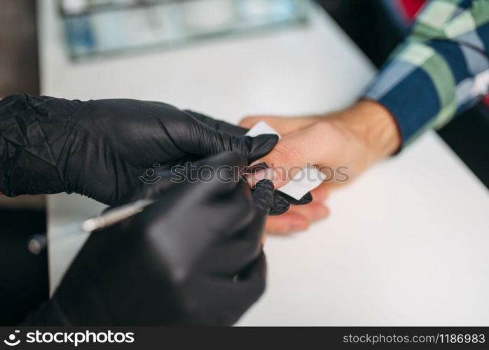 Female master in black gloves polishing nails to male client, top view, men manicure in salon. Manicurist doing hands care procedure. Master in gloves polishing nails to male client