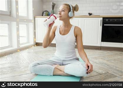 female mat with headphones drinking water