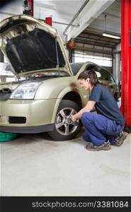 Female mechanic changing wheel of car with pneumatic torque wrench