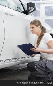 Female mechanic holding clipboard while examining car body at repair shop