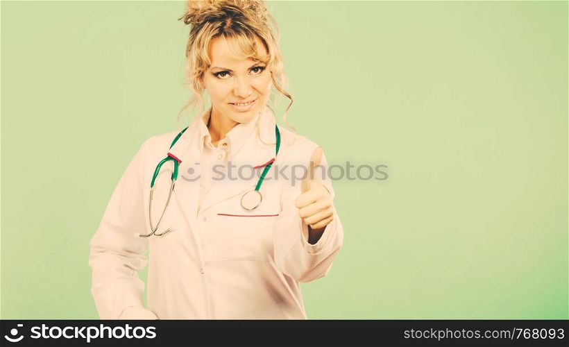 Female medical doctor showing thumb up. Woman in white professional uniform with stethoscope on neck. Middle aged successful pharmacist nurse on green.. Female doctor showing thumb up.