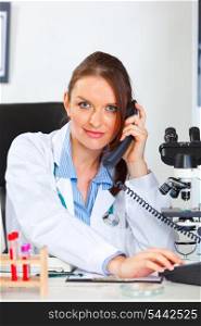 Female medical doctor sitting in cabinet and making phone call&#xA;