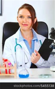 Female medical doctor sitting in cabinet with clipboard&#xA;