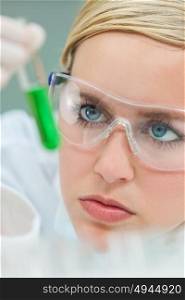 Female medical or research scientist or doctor using looking at a test tube of green solution in a lab or laboratory