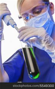 Female medical or scientific researcher or doctor using a pipette &amp; test tube of green solution in a laboratory