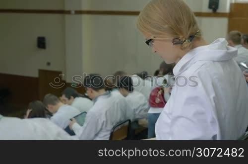 Female medical student using tablet computer on the lecture at the university or at the conference, then she turning to the camera and smiling