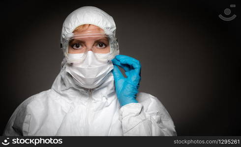 Female Medical Worker Wearing Protective Face Mask and Gear Against Dark Background.