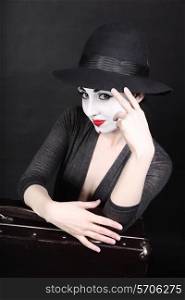 Female mime artist with theatrical makeup in hat and with suitcase