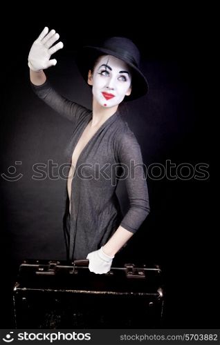 Female mime in white gloves with a suitcase, waving goodbye on a black background