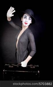 Female mime in white gloves with a suitcase, waving goodbye on a black background