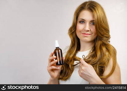 Female model with shiny wavy brown long hair using cosmetic, thermal protect spray. Treatment with oil essence, care and spa procedures. Smooth hairstyle.. Woman applying hair cosmetic