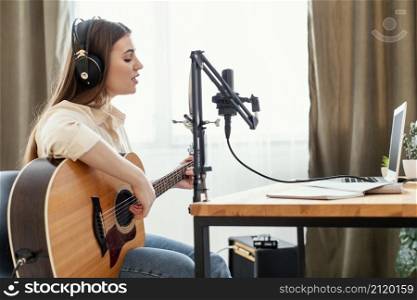female musician recording song home while playing acoustic guitar