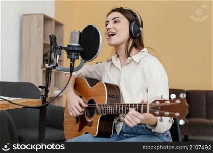 female musician recording song playing acoustic guitar home