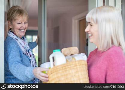 Female Neighbor Helping Senior Woman With Shopping Whilst Self Isolating During Coronavirus