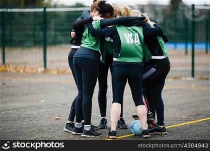 Female netball team in planning huddle on netball court