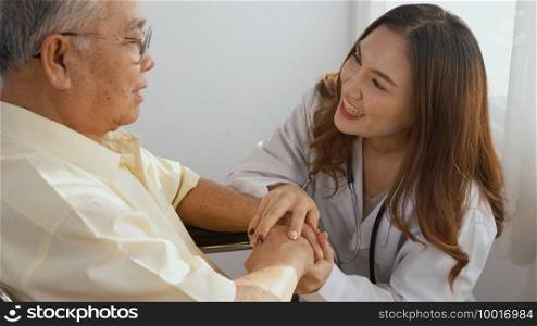 Female nurse doctor wear white uniform holding hand of patient senior or elderly old man during sit on wheelchair encourage and empathy at nursing hospital, older people healthcare support concept