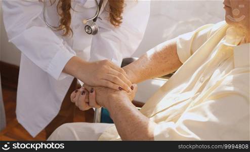 Female nurse doctor wear white uniform holding hand of patient senior or elderly old man during sit on wheelchair encourage empathy at nursing hospital, older people healthcare support